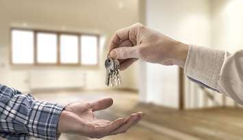 Realtor handing over keys to a house in an empty room. © Can Stock Photo / pbombaert