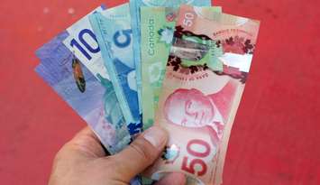 Several Canadian dollar bills are held up by someone's hand. Photo by Wirestock / iStock Editorial / Getty Images Plus via. Getty Images.