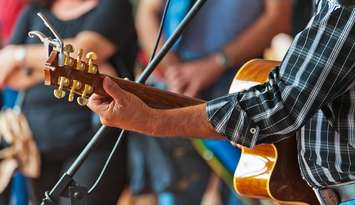 A musician busks with his acoustic guitar in the street as the crowd watches on. (File photo by NickRH/iStock / Getty Images Plus)