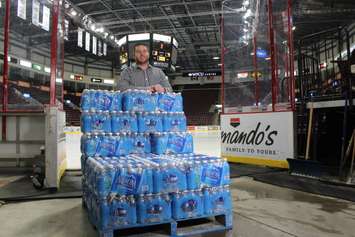 Coordinator of Fan Development Nathon Sellon poses with cases of bottled water donated to the teams water drive for Flint, January 20, 2016. (Photo by Maureen Revait) 