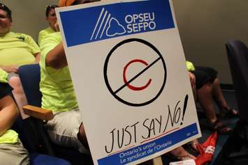 A sign held by a paramedic during a Chatham-Kent Council meeting, referencing a proposed blended service plan for Fire and EMS, 