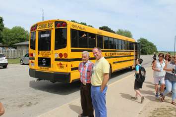 Jarrod Denure and 
 his father Ken pose behind the new electric bus as students from St. Anne Catholic School board.  June 15, 2018 (Photo by Greg Higgins)