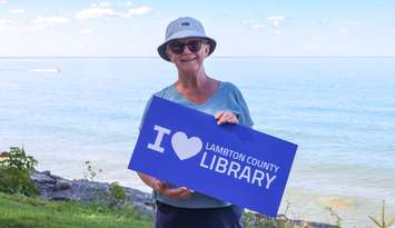 Library patron, Gwen Moore, holds an "I Love Lambton County Library" sign in Bright's Grove. October 2025. (Photo courtesy of Lambton County Library)