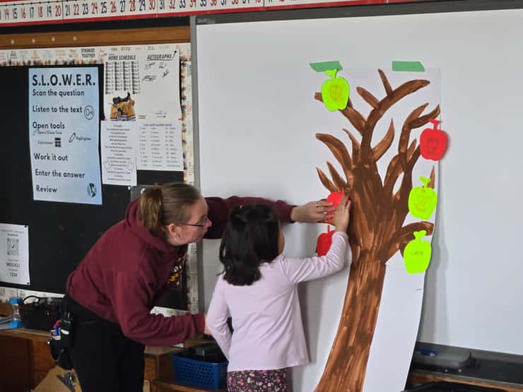 A Lansdowne student puts a paper apple on a tree at the Great Big Crunch - Mar. 26/26 (Blackburn Media Photo by Josh Boyce)