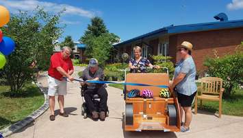 Lambton Shores Mayor Bill Weber (left) helps cut the ribbon at North Lambton Lodge in Forest, unveiling the site's new trishaw. July 30, 2019. (Photo by County of Lambton)